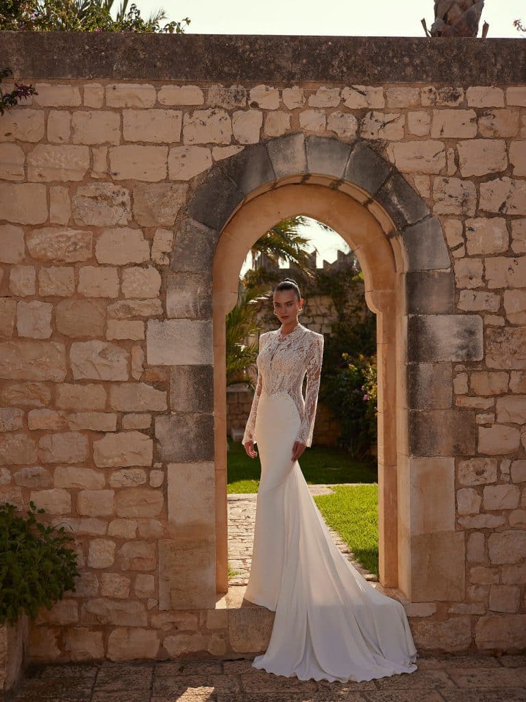 Trouwjurk Emmy met fit-and-flare silhouet, kant, pailletten, doorschijnende kantmouwen en illusie rug met knopen voor een verfijnde en betoverende uitstraling.